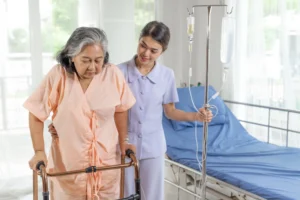 nurse helping elderly woman with walker and IV in hospital room