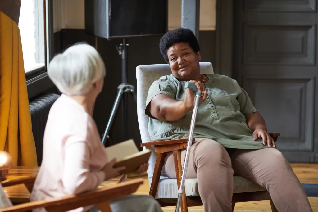 Senior woman using a cane talking with a friend in a cozy living room while receiving emotional support