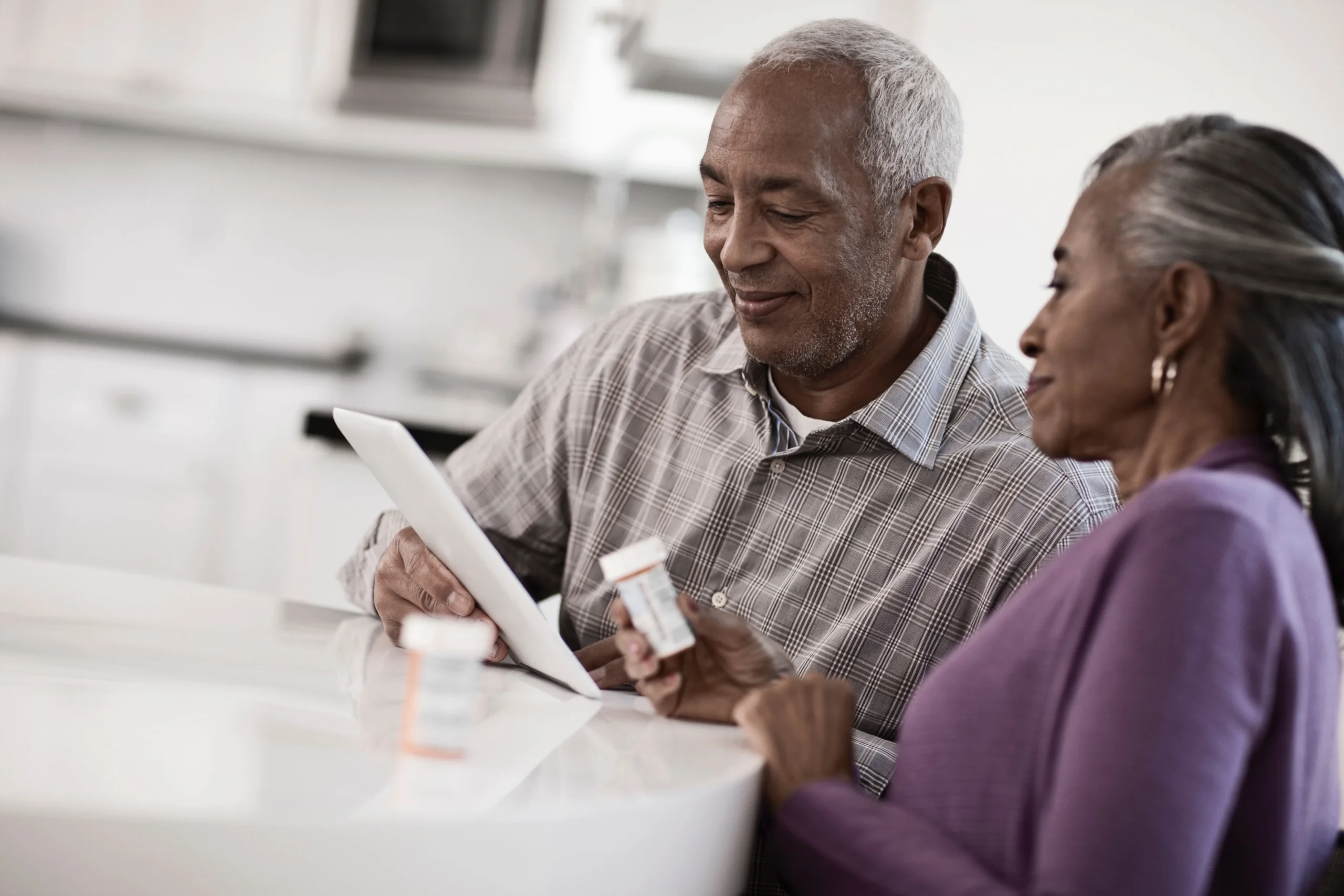 Senior couple reviewing medication instructions at home with pill bottles and a digital tablet.