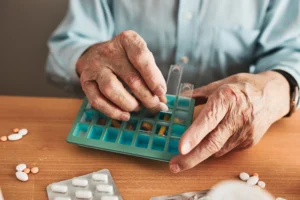 Older adult organizing prescription pills into a weekly pill organizer for proper medication management.