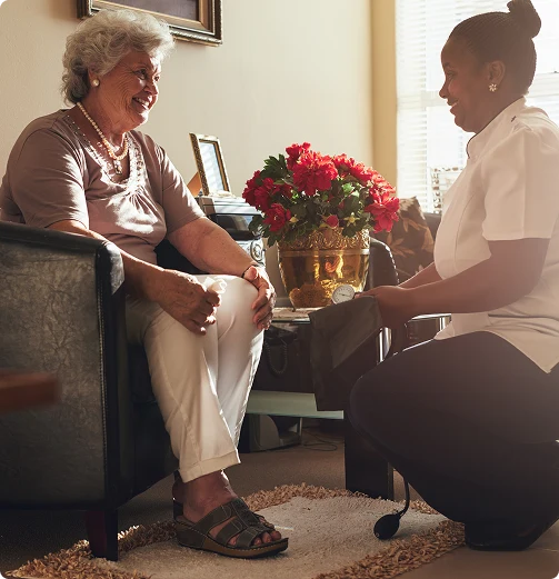 Caregiver sitting and talking with elderly woman in living room during in-home care visit