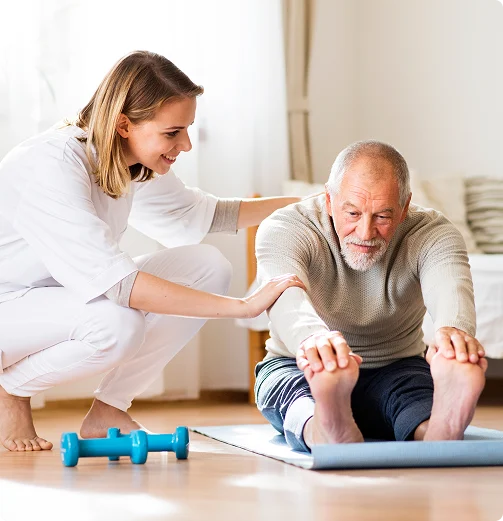 Physiotherapist guiding senior man through seated stretching exercise on mat as part of mobility rehabilitation