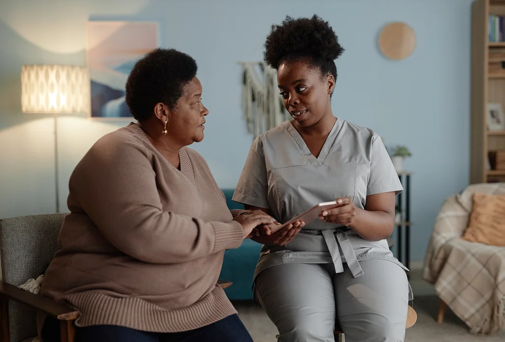 Nurse showing medical information on tablet to senior woman during in-home care consultation