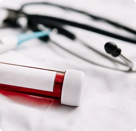 Blood sample tube and stethoscope on medical surface, clinical healthcare equipment close-up