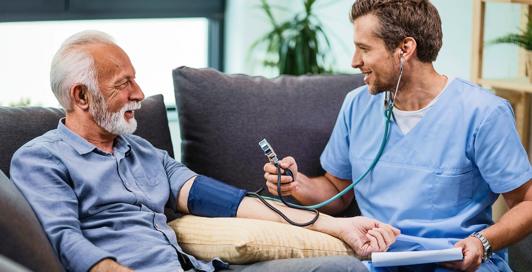 Caregiver checking blood pressure of an elderly man at home using a monitor