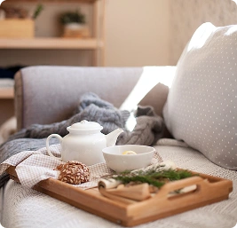 Breakfast tray with tea, pastry, and herbs placed on a cozy bed in a bright bedroom