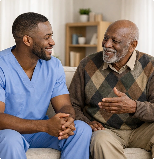 Caregiver talking with a smiling elderly man while sitting together on a sofa