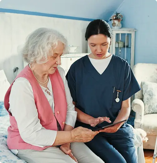 Caregiver showing a tablet to an elderly woman at home.