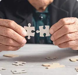 Elderly person holding two puzzle pieces together.