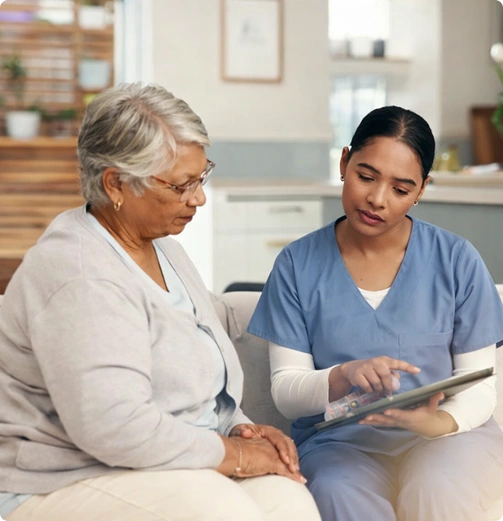 Caregiver showing information on a tablet to an elderly woman during a home care visit