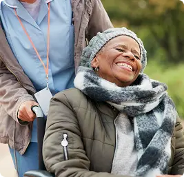 Caregiver pushing a joyful elderly woman in a wheelchair outdoors