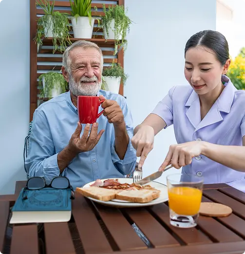 Caregiver helping an elderly man with breakfast on an outdoor patio