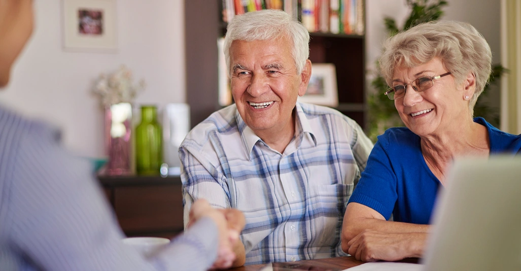 Smiling senior couple shaking hands with a care advisor during a home consultation