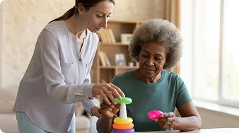 Caregiver assisting an elderly woman with a colorful stacking toy during a cognitive activity at home.