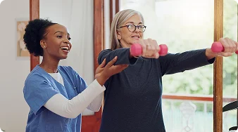 Physical therapist helping a senior woman perform arm strengthening exercises with dumbbells.
