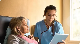 Nurse using a stethoscope to examine an elderly woman while reviewing medical information on a tablet.