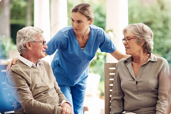 Home care nurse providing compassionate support to a senior couple during an outdoor conversation.