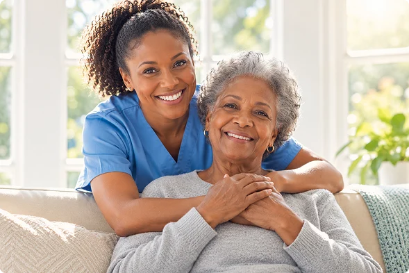 Smiling caregiver embracing a happy senior woman while providing compassionate home care and support.