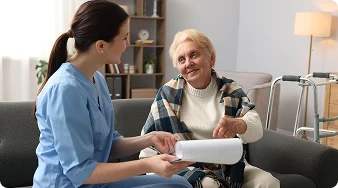 Home care nurse reviewing medical documents with a smiling elderly woman.