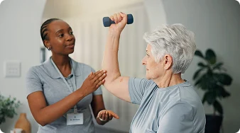 Physical therapist assisting a senior woman with arm strengthening exercises using a dumbbell.
