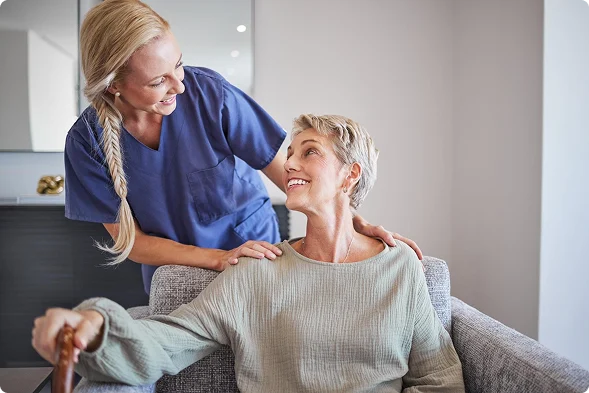 Female caregiver smiling and providing support to a senior woman at home.